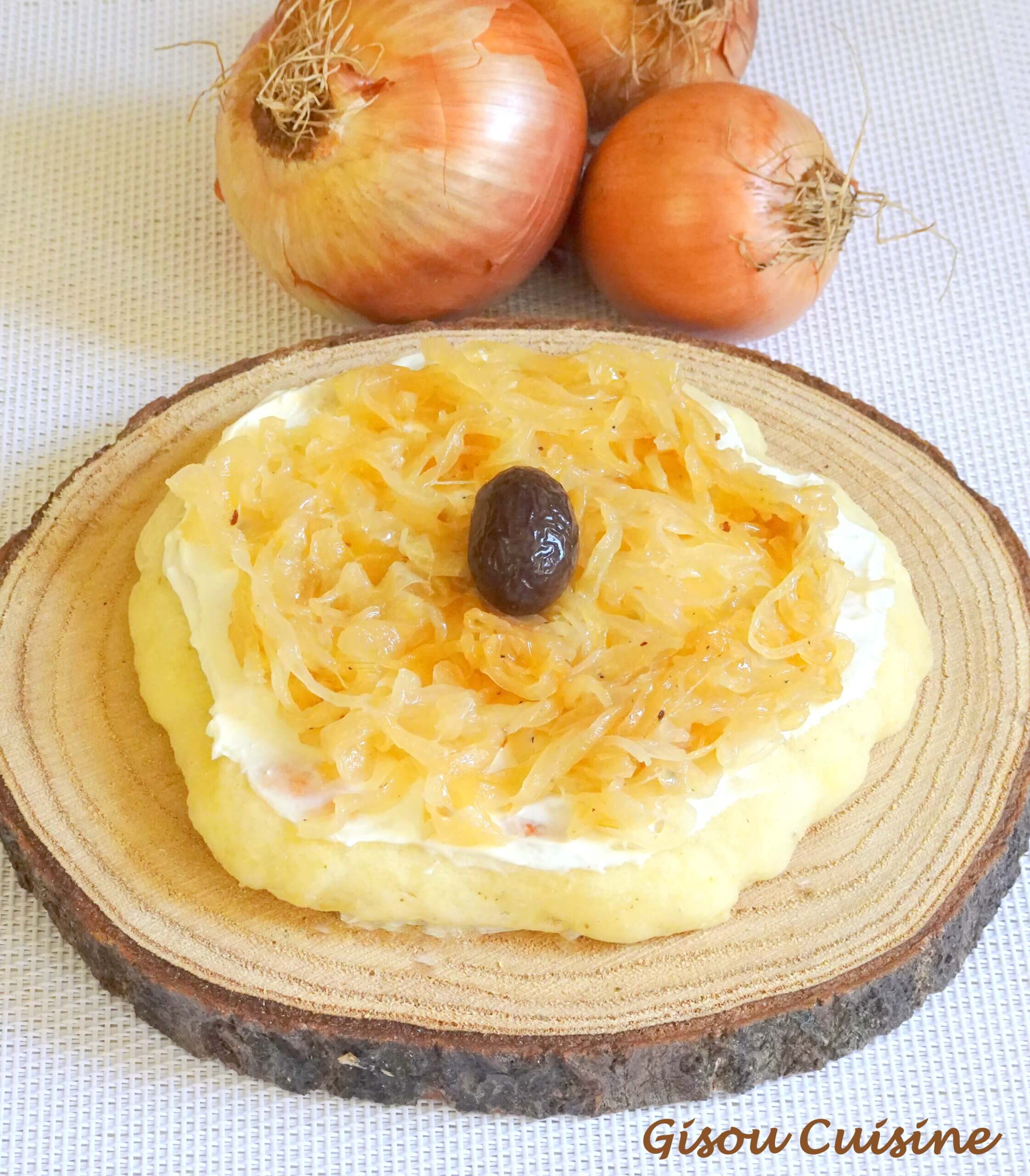 pain au yaourt et confit oignon coupé posé sur un rondin en bois. En arrière plan 3 oignons jaunes.